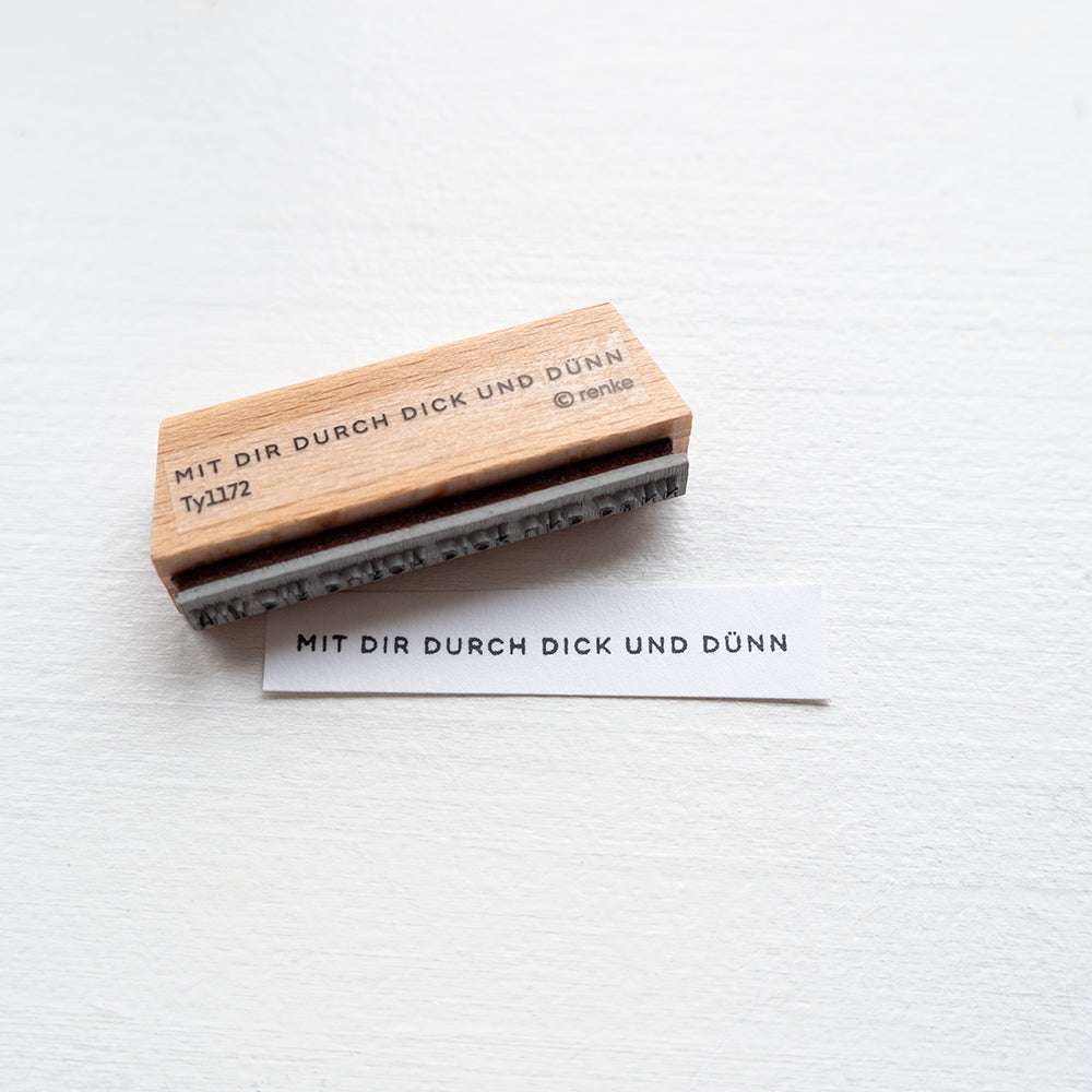 Holzstempel von Alexandra Renke mit deutschem Text "MIT DIR DURCH DICK UND DÜNN" sowie Stempelgummi-Abdruck auf Papierstreifen - ideal für kreative Papierprojekte.