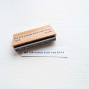 Holzstempel von Alexandra Renke mit deutschem Text "MIT DIR DURCH DICK UND DÜNN" sowie Stempelgummi-Abdruck auf Papierstreifen - ideal für kreative Papierprojekte.