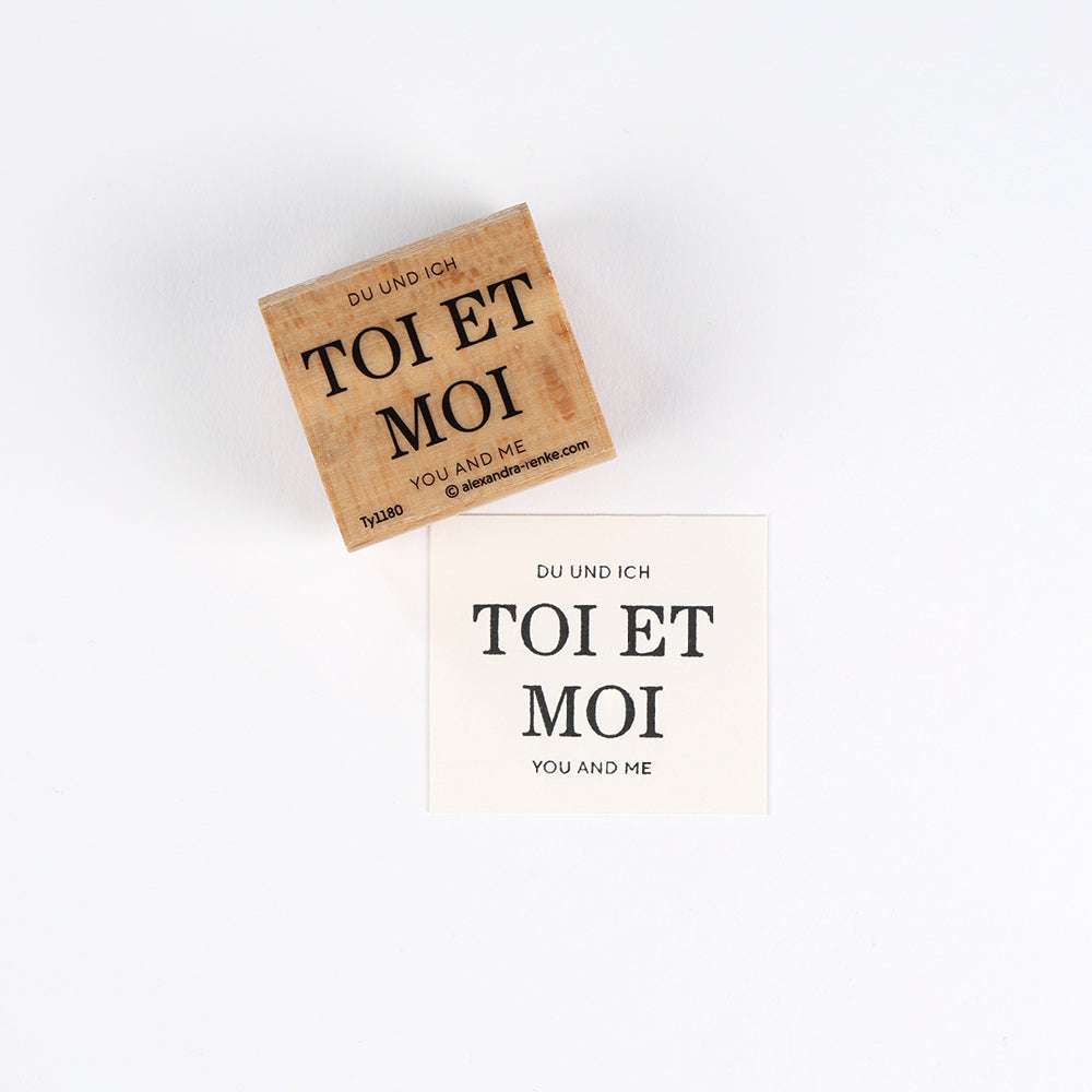 Ein Alexandra Renke Holzstempel und eine gestempelte Karte mit "TOI ET MOI, YOU AND ME" in Deutsch, Französisch und Englisch - ideal für Papierprojekte mit hochwertigem Stempelgummi.