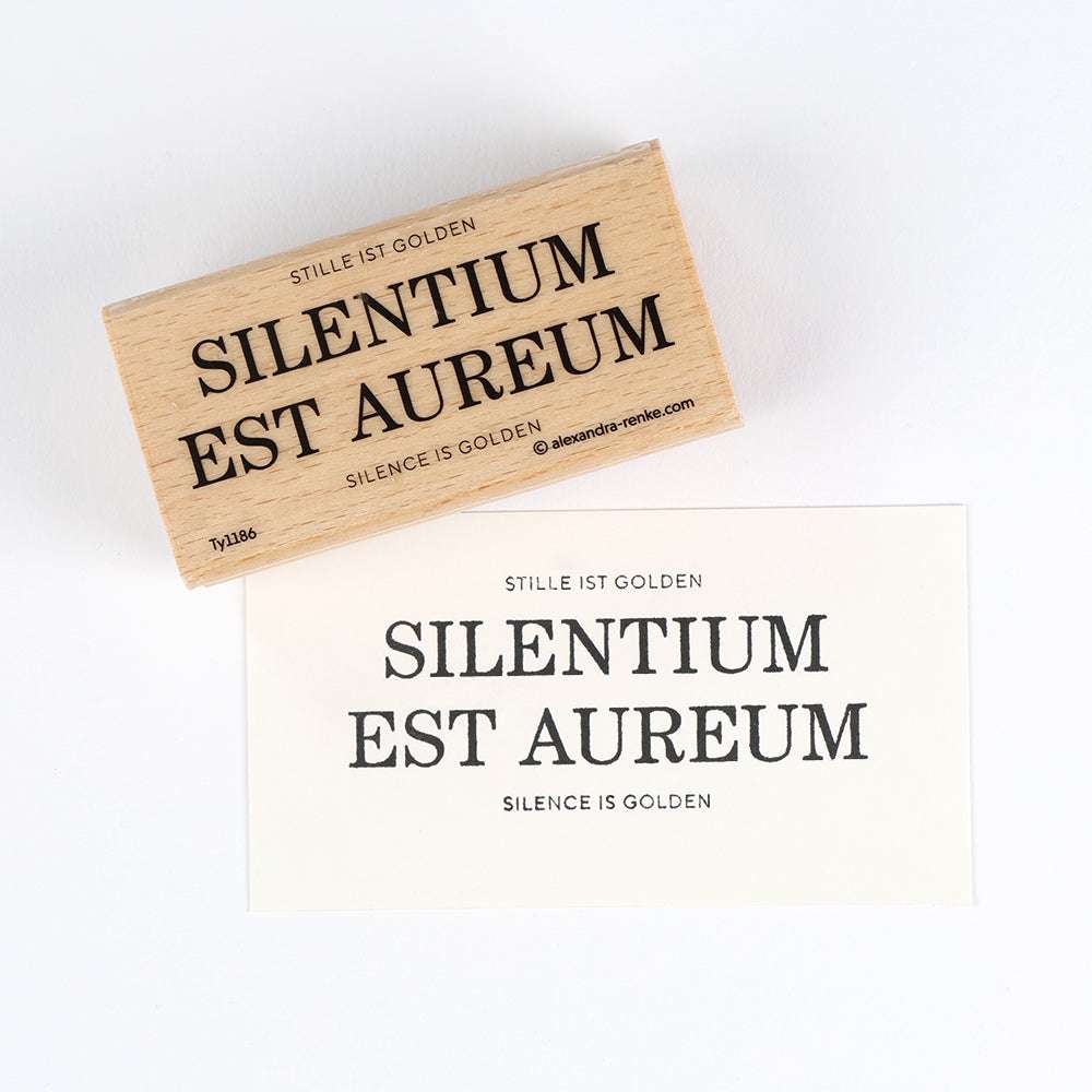 Alexandra Renke bietet einen hochwertigen Holzstempel und Papier an, die beide mit "Silencium Est Aureum" und seinen Übersetzungen und detailreichen Motiven für eine elegante Note sorgen.