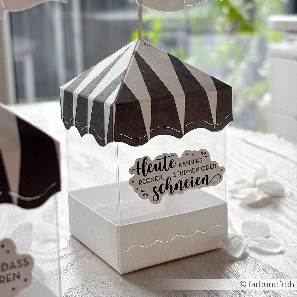 Alexandra Renke schwarz-weiß gestreifte zeltförmige Pappschachtel mit deutschem Text und Stempelmotiv an der Seite, ausgestellt auf einem Leuchttisch.