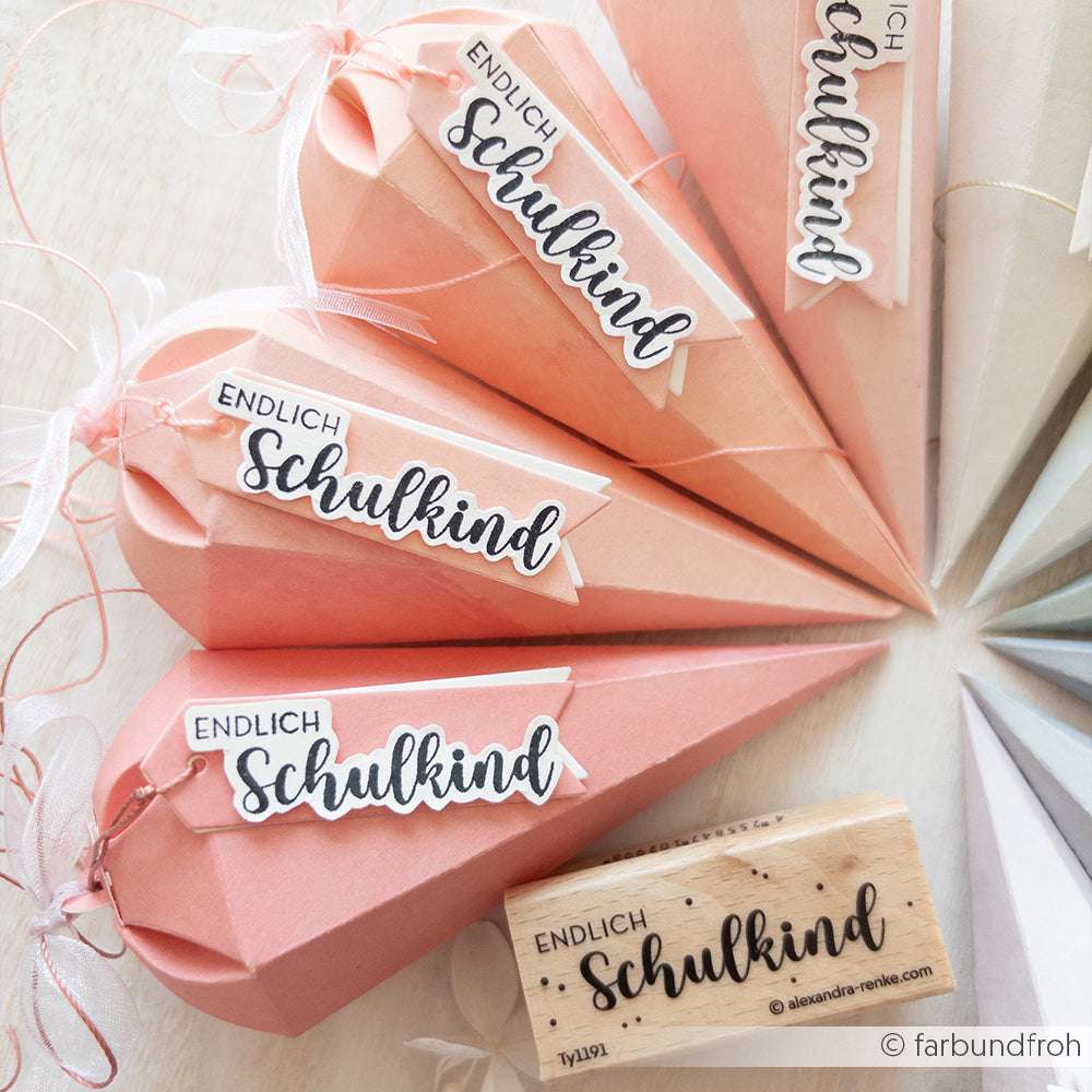 Vier rosafarbene Papiertüten mit "Endlich Schulkind"-Anhängern und einem Holzstempel von Alexandra Renke ruhen auf einer hellen Fläche, die aus hochwertigen Materialien gefertigt ist.