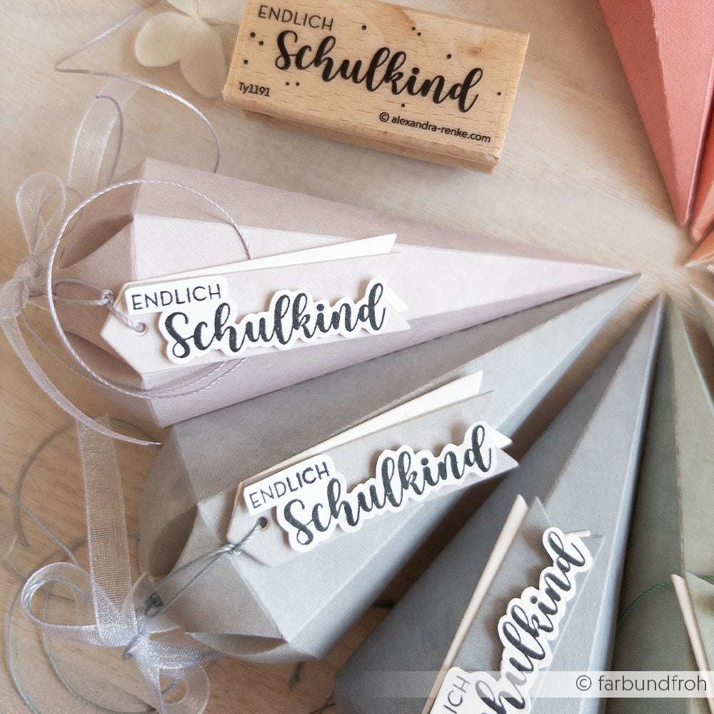 Geschenktüten und ein Holzstempel mit der Aufschrift "Endlich Schulkind" von Alexandra Renke, arrangiert auf einer hellen Fläche mit Bandakzenten und gefertigt aus hochwertigen Materialien.