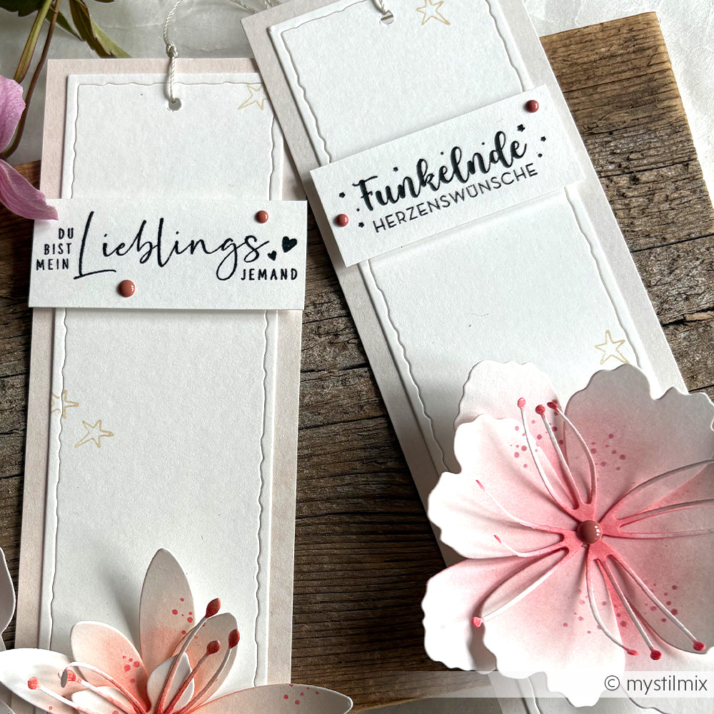 Zwei handgefertigte Alexandra Renke-Lesezeichen mit deutschem Text, rosafarbenen Blumen und Stern-Akzenten auf einer Holzoberfläche - perfekt für Papierprojekte, hergestellt mit Holzstempeln und bunten Stempelkissen.