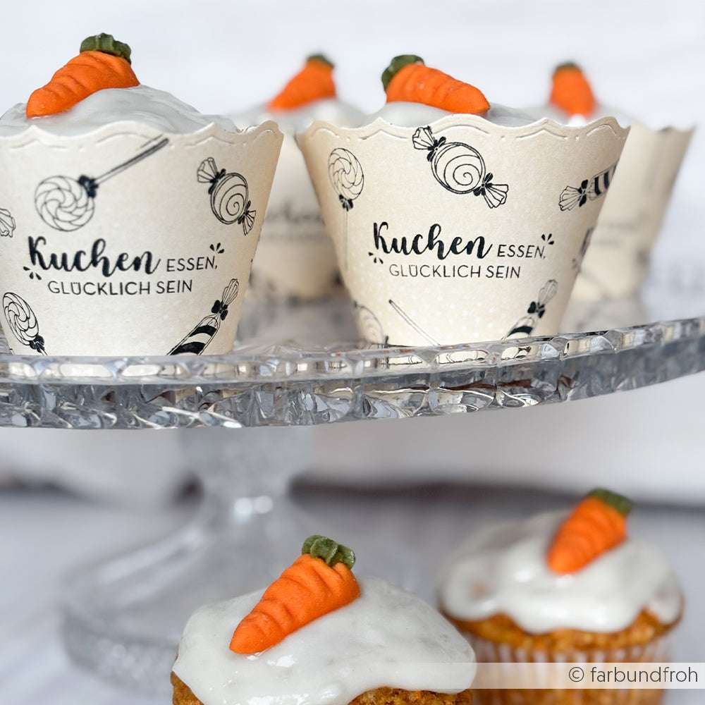 Cupcakes mit weißem Zuckerguss und Karottenverzierung auf einem Glasständer in dekorativen Papierbechern - perfekt für Alexandra Renke Papierprojekte oder in Kombination mit einem Holzstempel für eine charmante, handwerkliche Note.