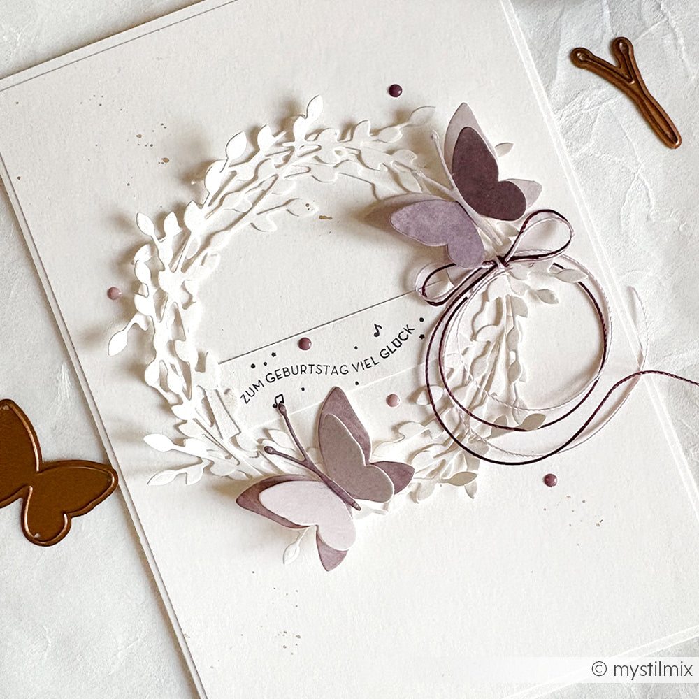 Handgemachte Geburtstagskarte von Alexandra Renke mit Papierschmetterlingen, einem Kranz und einem deutschen Geburtstagsgruß, gestempelt mit einem Holzstempel auf weißem Hintergrund.