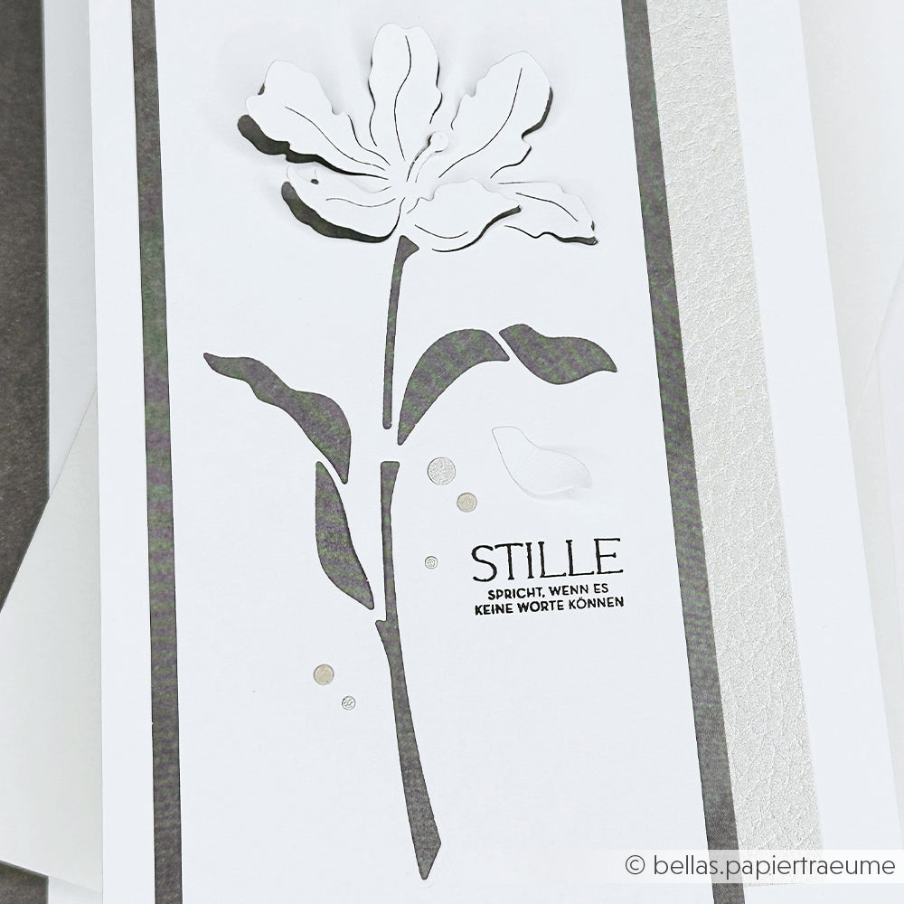 Weiße Karte von Alexandra Renke mit schwarzer Blumensilhouette, kleinem Vogel und deutschem Text "STILLE spricht, wenn es keine Worte kann." Ideal für Papierprojekte mit Holz- oder Gummistempeln.