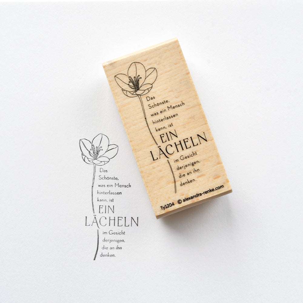 Der Alexandra Renke Holzstempel erstellt ein deutsches Zitat mit schwarzer Tinte und einer Blumenillustration - ideal für Papierprojekte und kreative Gestaltungen.
