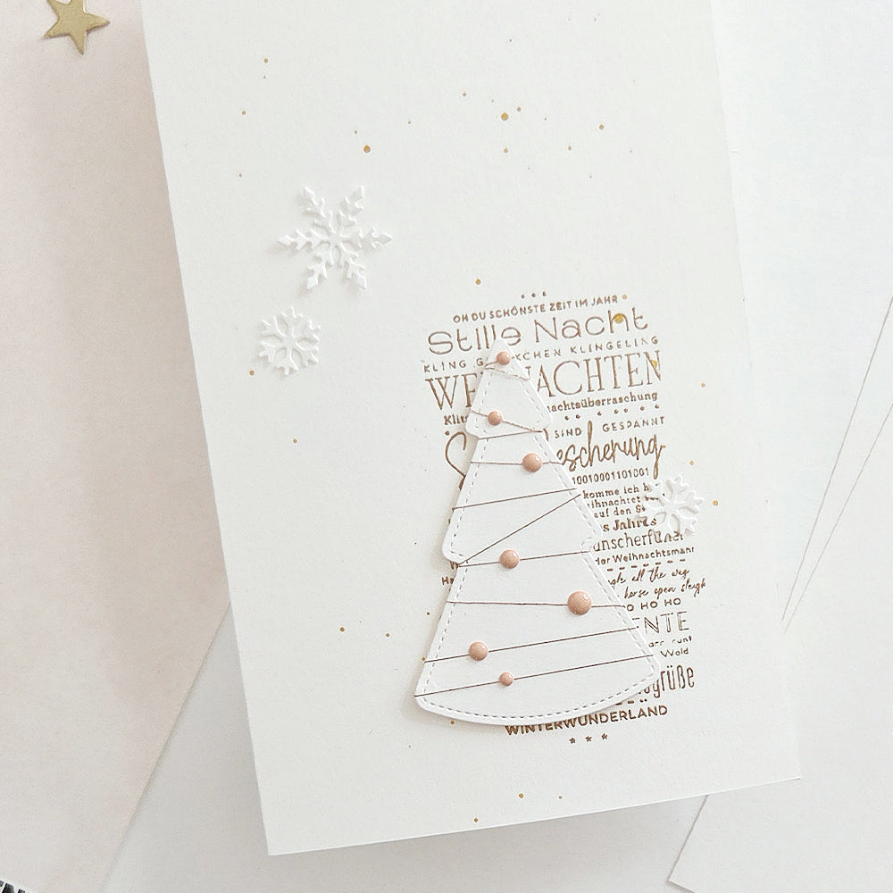 Weihnachtskarte mit einem ausgestanzten Papierbaum, verziert mit Schneeflocken und Holzstempeln.