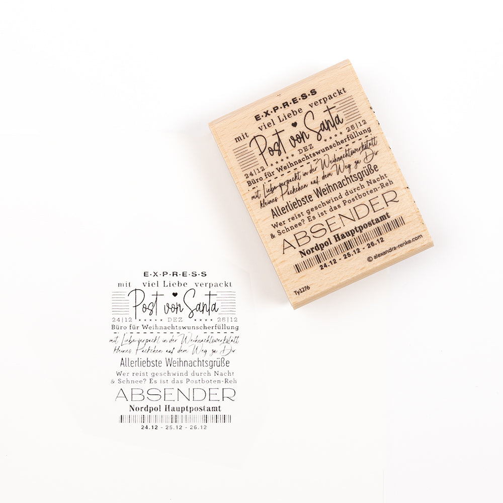 Ein Holzstempel und sein Stempelabdruck mit der Aufschrift „Post von Santa“ – ein deutscher Text zum Thema Weihnachten aus dem Postamt am Nordpol.