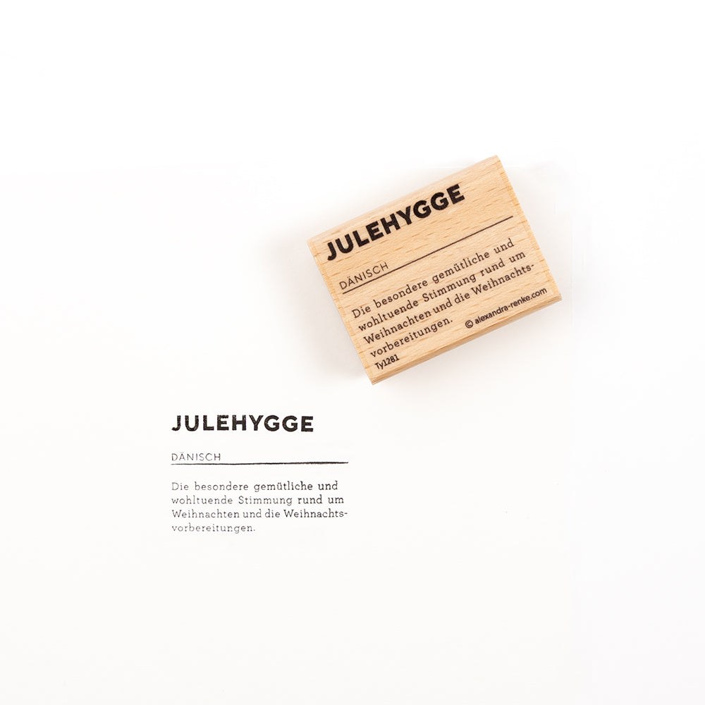 Ein „JULEHYGGE“-Holzstempel neben seinem Abdruck auf weißem Hintergrund, der das Design des Holzstempels zeigt.