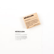 Ein Holzstempel und eine bedruckte Karte mit dem Wort „Réveillon“ und dessen Definition – perfekt für Papierprojekte.