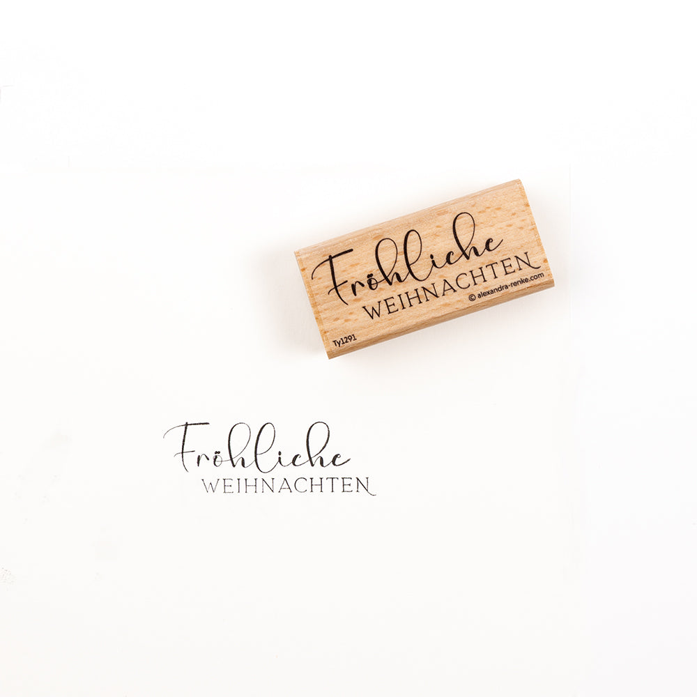 Ein Holzstempel und sein Stempelabdruck mit der Aufschrift „Fröhliche Weihnachten“.
