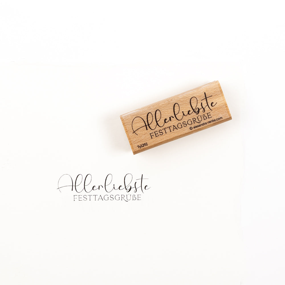 Holzstempel mit einer Gummiplatte mit der Aufschrift „Allerliebste FESTTAGSGRÜBE“ und einem Musterabdruck darunter.