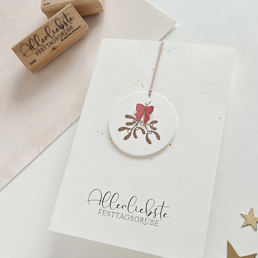 Grußkarte mit einem Mistelzweig-Motiv und dem Text Allerliebste Festtagsgrüße im Holzstempel-Stil.