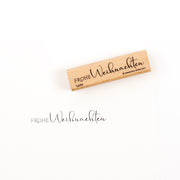 Ein Holzstempel mit der Aufschrift „Frohe Weihnachten“ und dem dazugehörigen Stempelabdruck darunter.