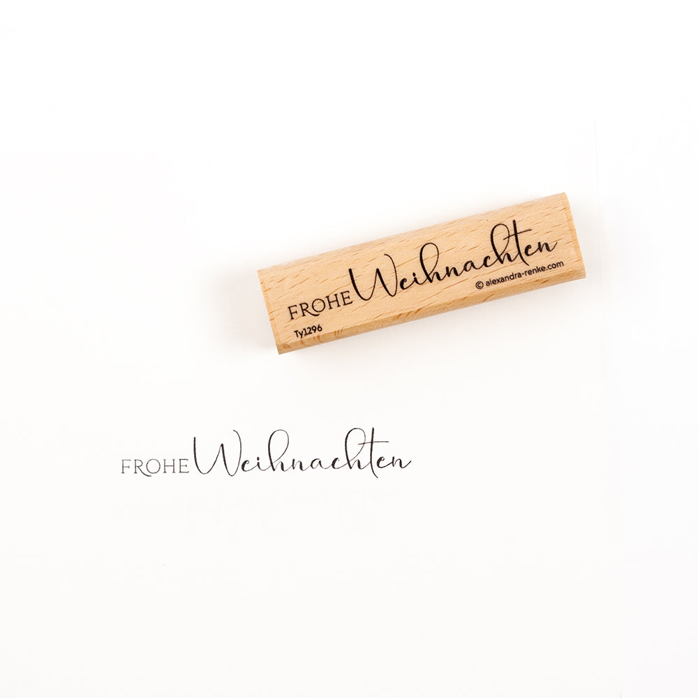 Ein Holzstempel mit der Aufschrift „Frohe Weihnachten“ und dem dazugehörigen Stempelabdruck darunter.