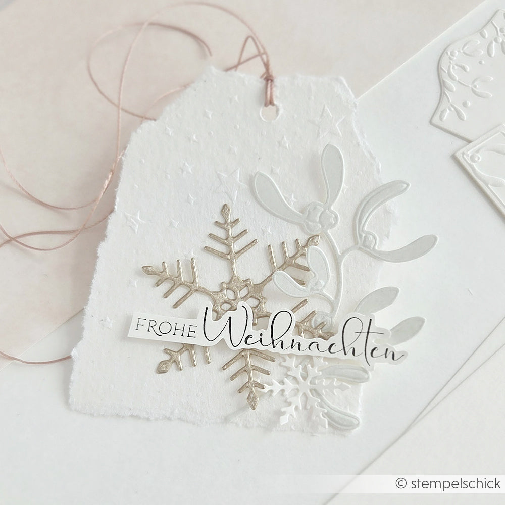 Handgefertigter Geschenkanhänger mit einer Schneeflocke, Mistelzweig und einem Frohe Weihnachten-Holzstempel-Motiv.