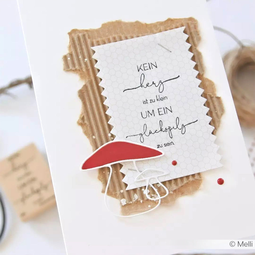 Eine handgemachte Karte von Alexandra Renke mit deutschem Text, rotem Papierpilz, strukturiertem braunem Papier und Holzstempel-Akzenten - ideal für einzigartige Papierprojekte auf weißem Hintergrund.