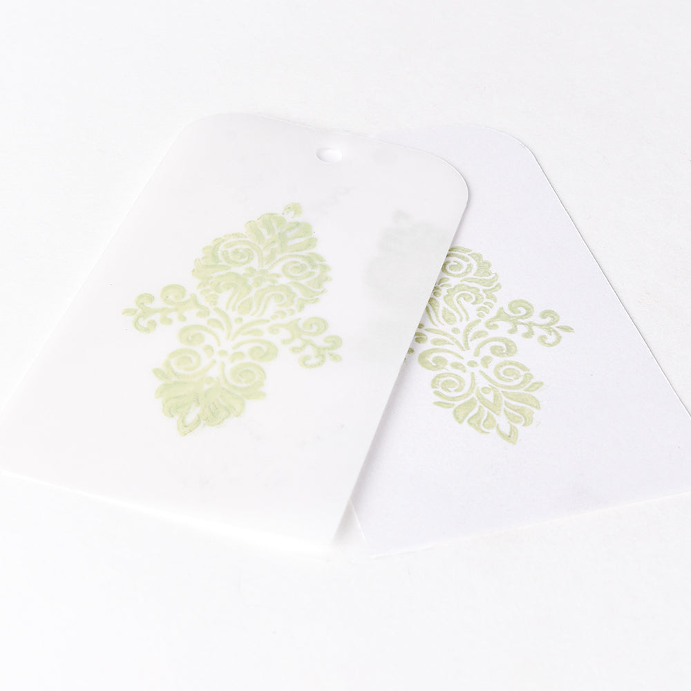 Zwei weiße Karten mit verschlungenen hellgrünen Blumenmustern, die sich teilweise überlappen, zeigen wunderschöne Stempelergebnisse, die mit Tsukineko Versa Magic Stempelkissen erstellt wurden.