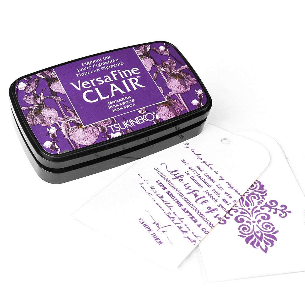 Tsukineko VersaFine Clair Purple Stempelkissen mit floralem Muster, daneben zwei weiße, mit Pigment-Tinten gestempelte Anhänger.