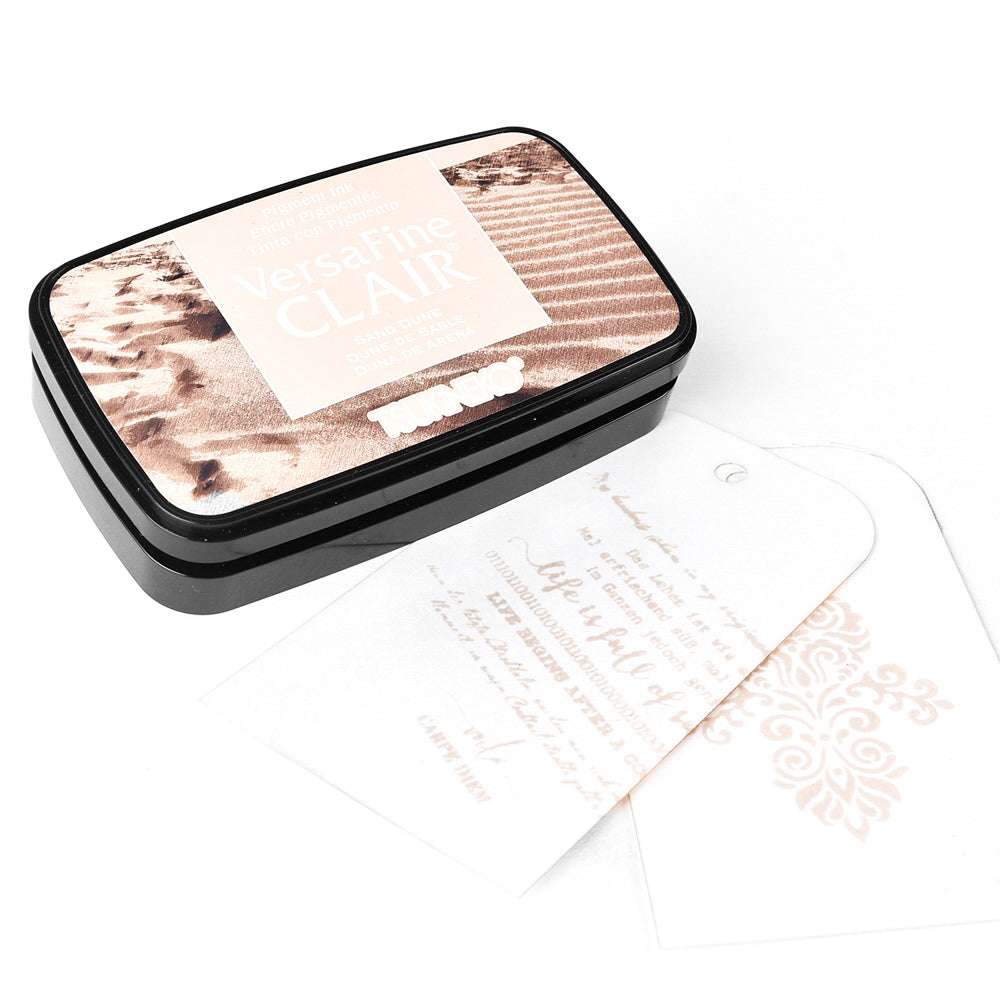 Ein Tsukineko VersaFine Clair Stempelkissen in Acorn-Farbe mit zwei weißen, bestmpelten Papieranhängern daneben.