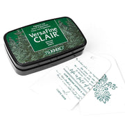 Ein Tsukineko VersaFine Clair Stempelkissen in Grün wird mit zwei verzierten weißen Anhängern daneben ausgestellt.