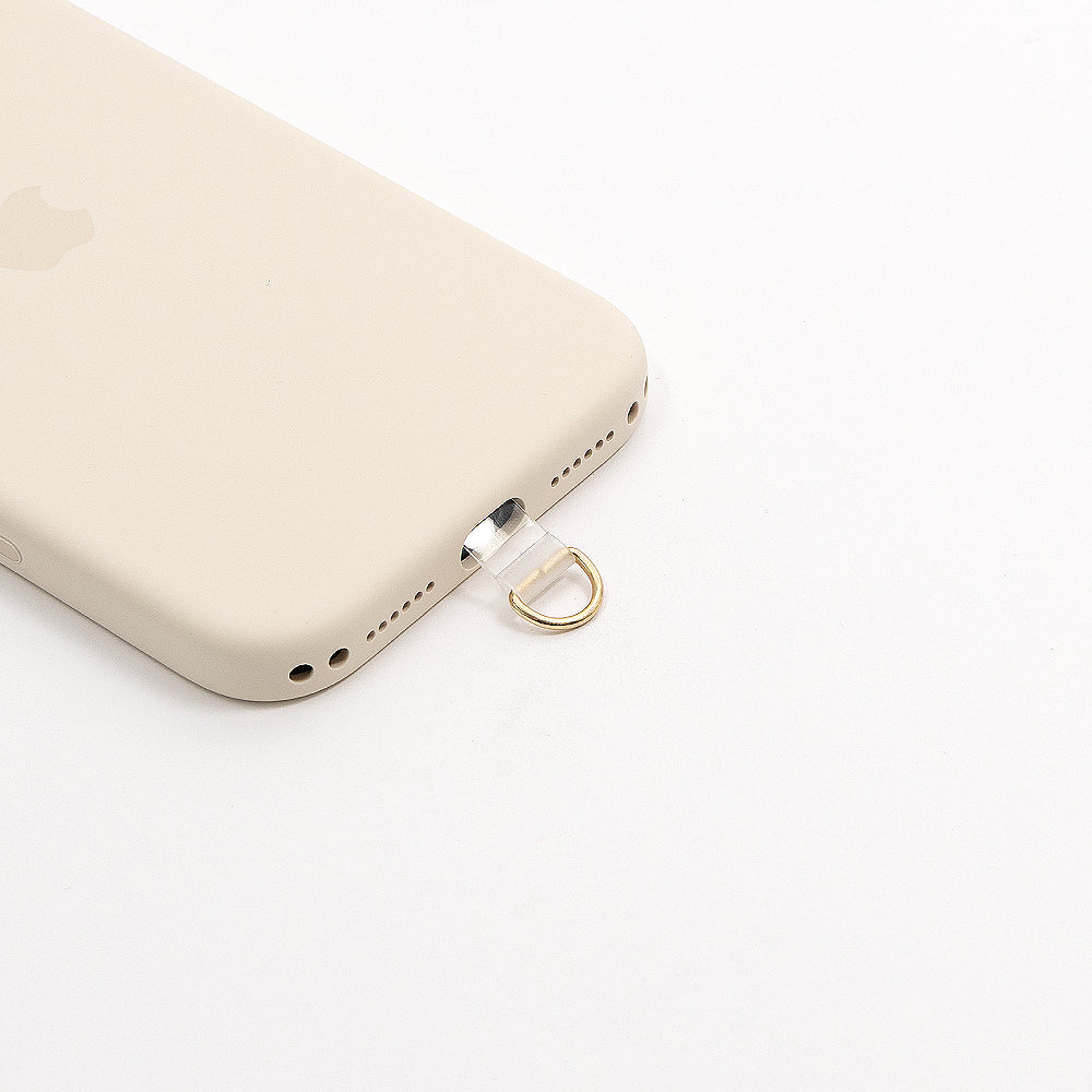 Eine beigefarbene Handyhülle von Alexandra Renke verfügt über einen kleinen goldenen Schlüsselring, der in den Ladeanschluss passt – perfekt für alle, die praktisches Smartphone-Zubehör suchen oder einen Handy-Patch an einer Handykette befestigen möchten.