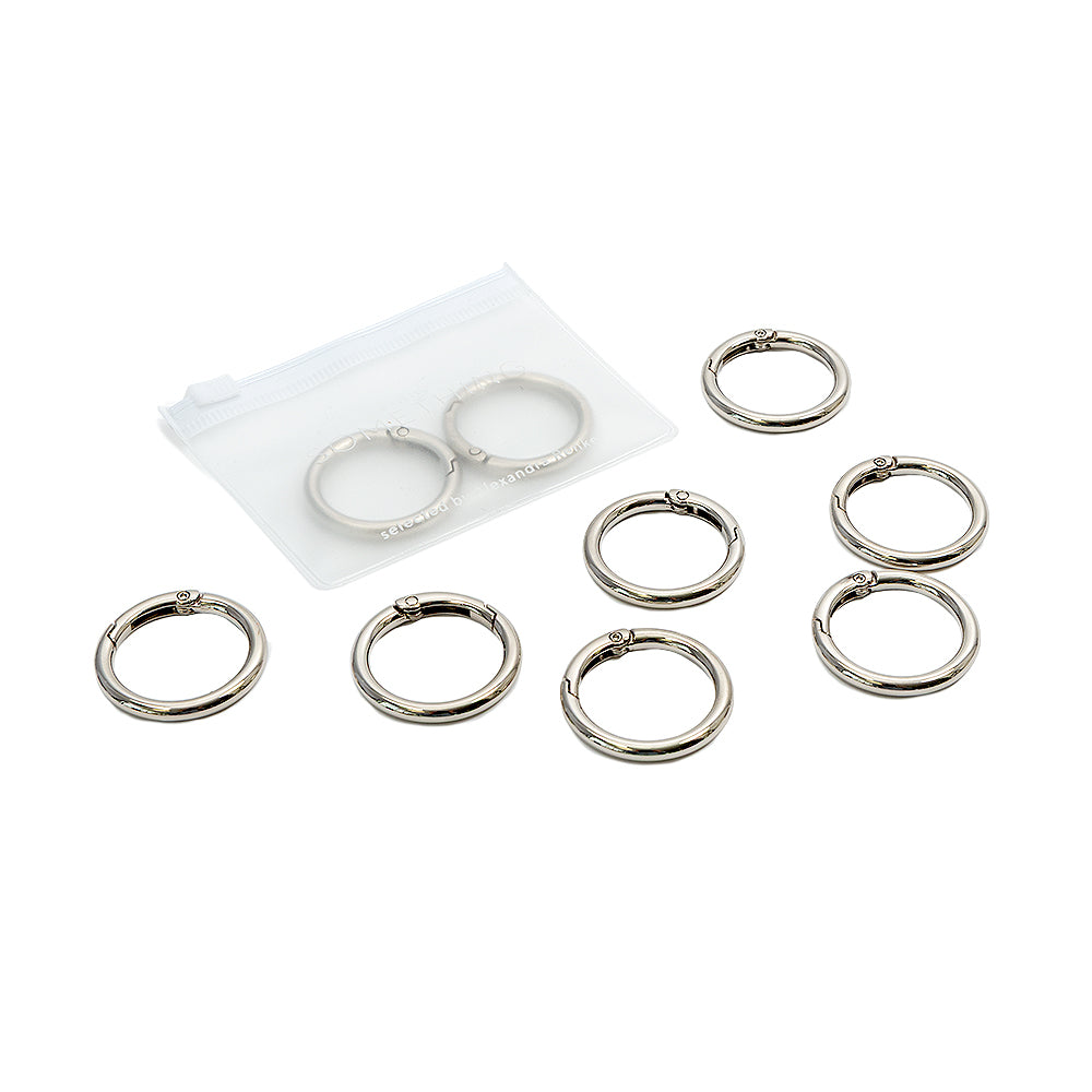 Acht silberne Ringbinderringe von Alexandra Renke, sechs außen und zwei in einem durchsichtigen Beutel mit Reißverschluss, auf weißem Hintergrund – ideal für DIY-Projekte oder zum Befestigen an Handyketten mit einem sicheren Karabinerhaken.