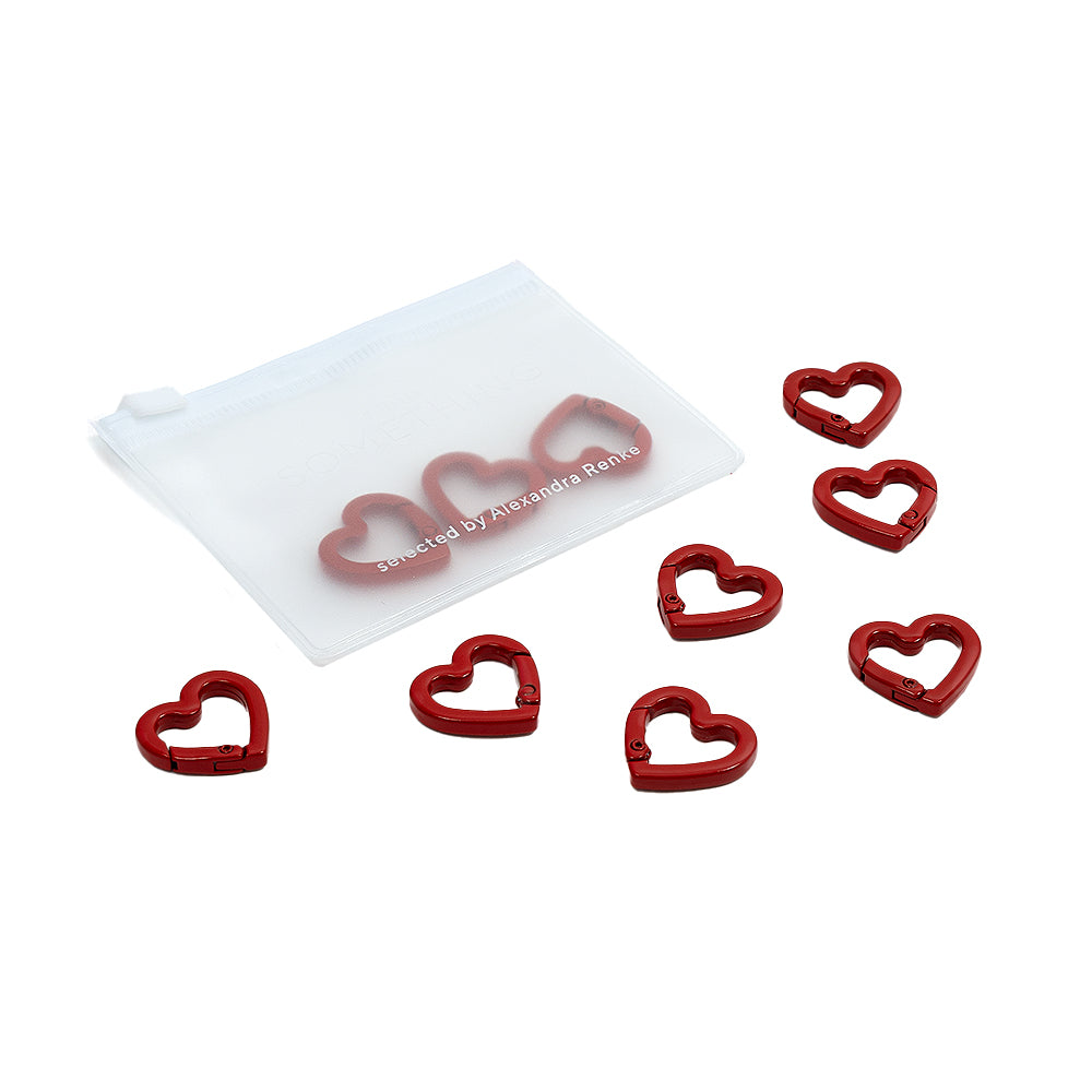 Sieben rote, herzförmige „Alexandra Renke Herz-Karabiner“-Clips, zusammen mit einem weißen Beutel, angeordnet auf weißem Hintergrund – ideal für DIY-Projekte oder zum Basteln eigener, einzigartiger Handy-Anhänger.