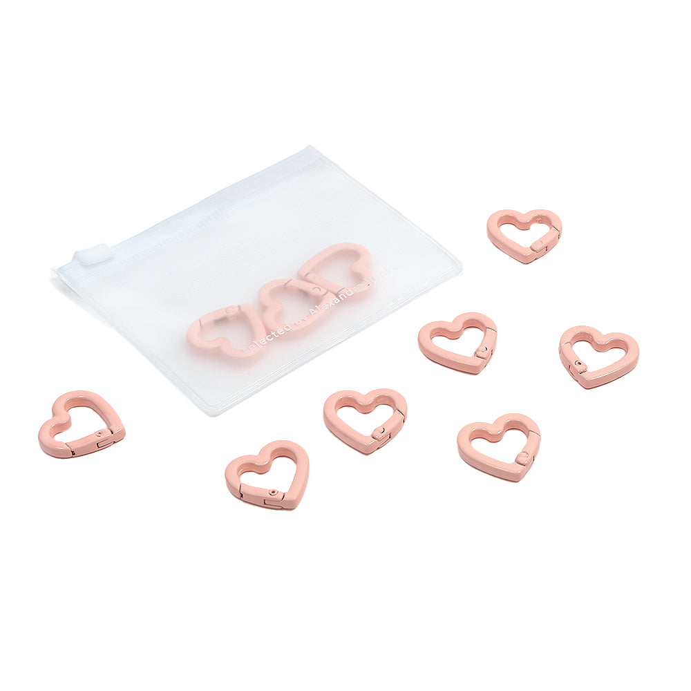 Acht rosa, herzförmige Clips von Alexandra Renke, ideal für Handyketten oder andere kreative DIY-Projekte, präsentiert in einem weißen Beutel mit Reißverschluss vor weißem Hintergrund.
