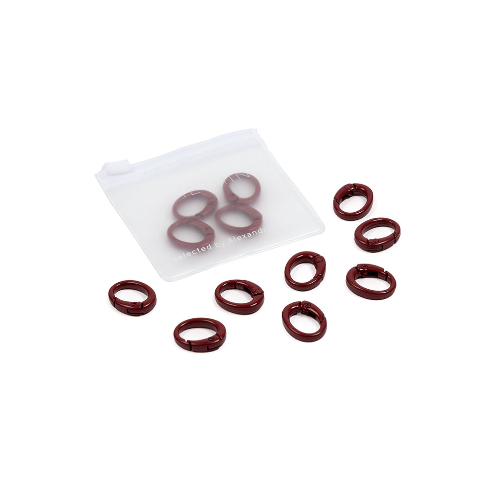 Neun kastanienbraune ovale Ringe (Ovale Karabiner) und ein kleines, mattiertes Reißverschluss-Säckchen auf weißem Hintergrund – perfekt zum Basteln eigener Handyketten oder Schlüsselbänder.