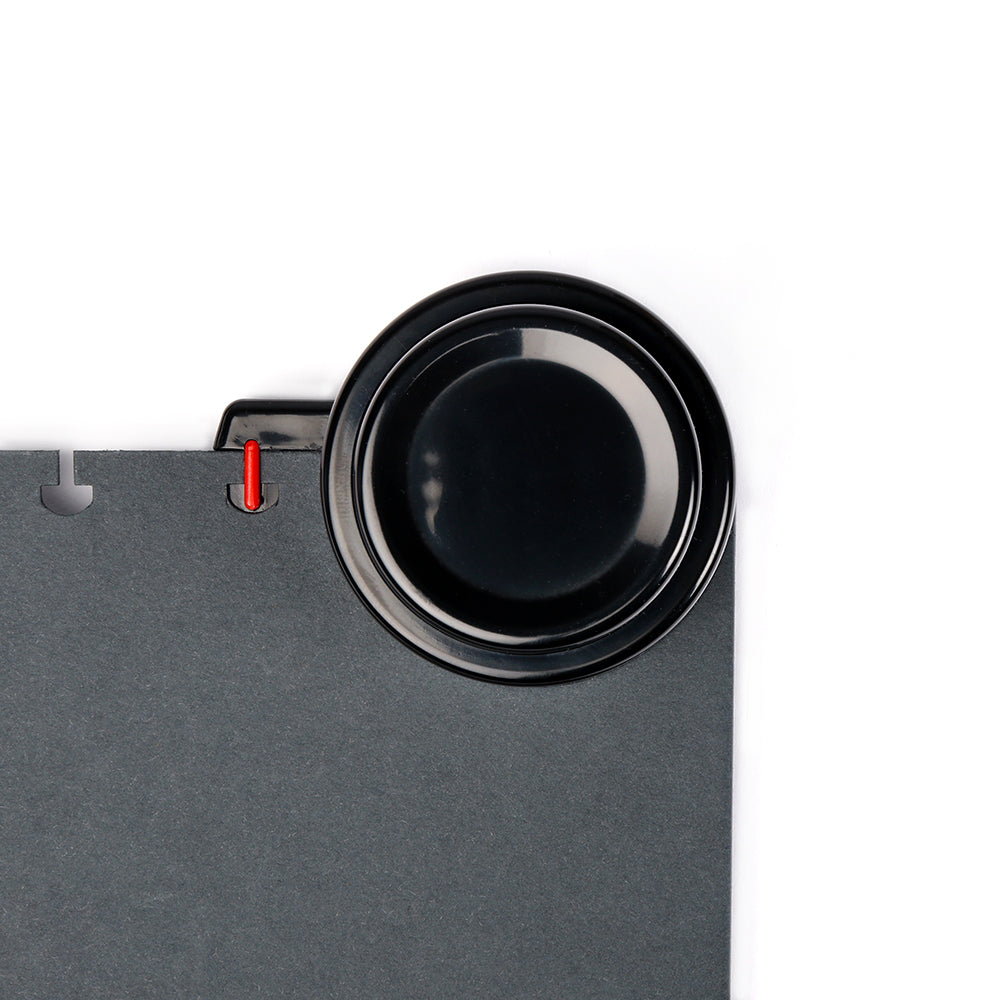 Eine schwarze Platte auf einer dunkelgrauen Oberfläche hält rote und weiße Bindeklammern und einen Alexandra Renke Stanzer für Bindescheiben, perfekt für Ihr nächstes Buchbindeprojekt - alles vor einem weißen Hintergrund.