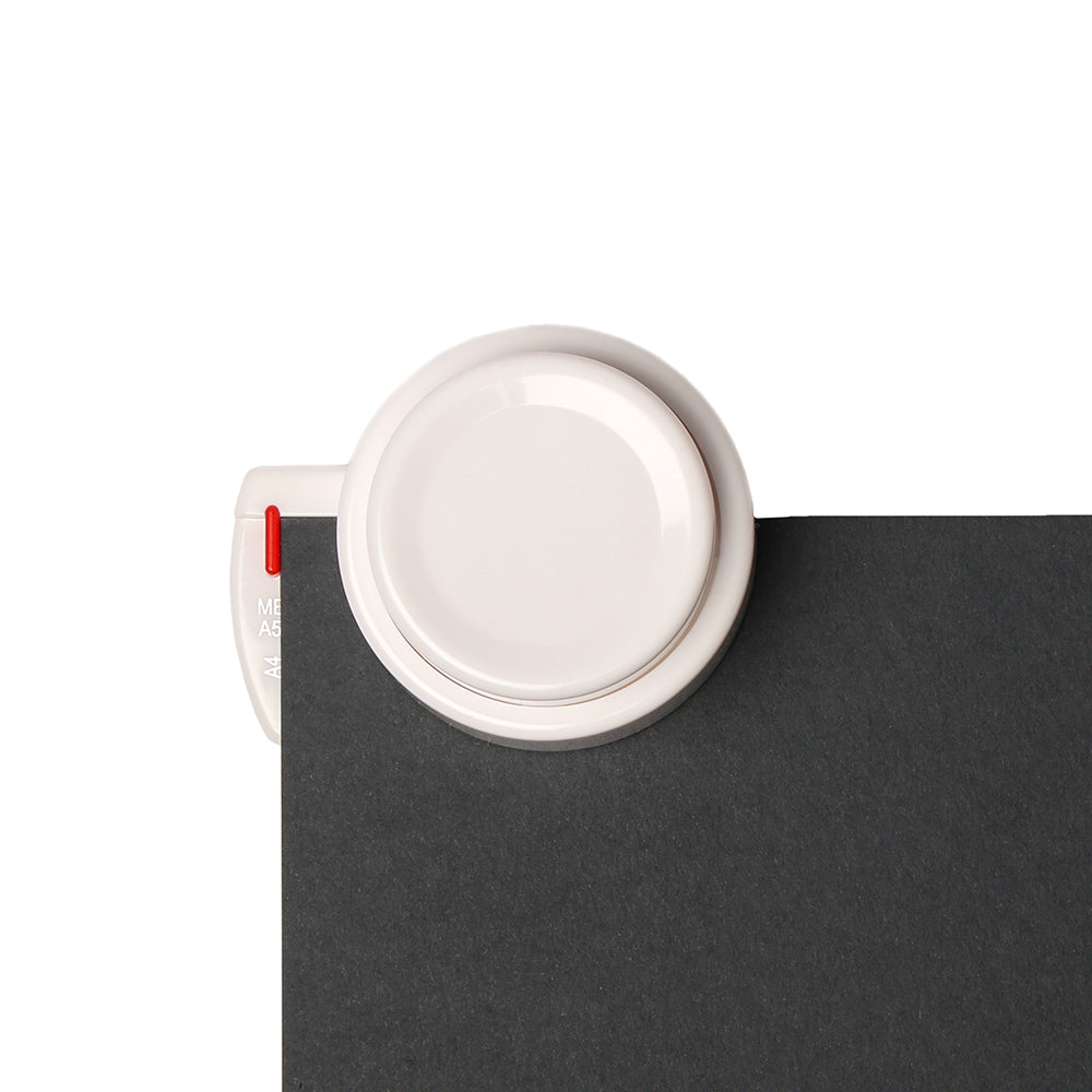 Ein weißer, runder Alexandra Renke Stanzer für Bindescheiben Clip ist an der Ecke eines schwarzen Blattes auf weißem Hintergrund befestigt, ideal für Ihr nächstes Buchbindeprojekt.