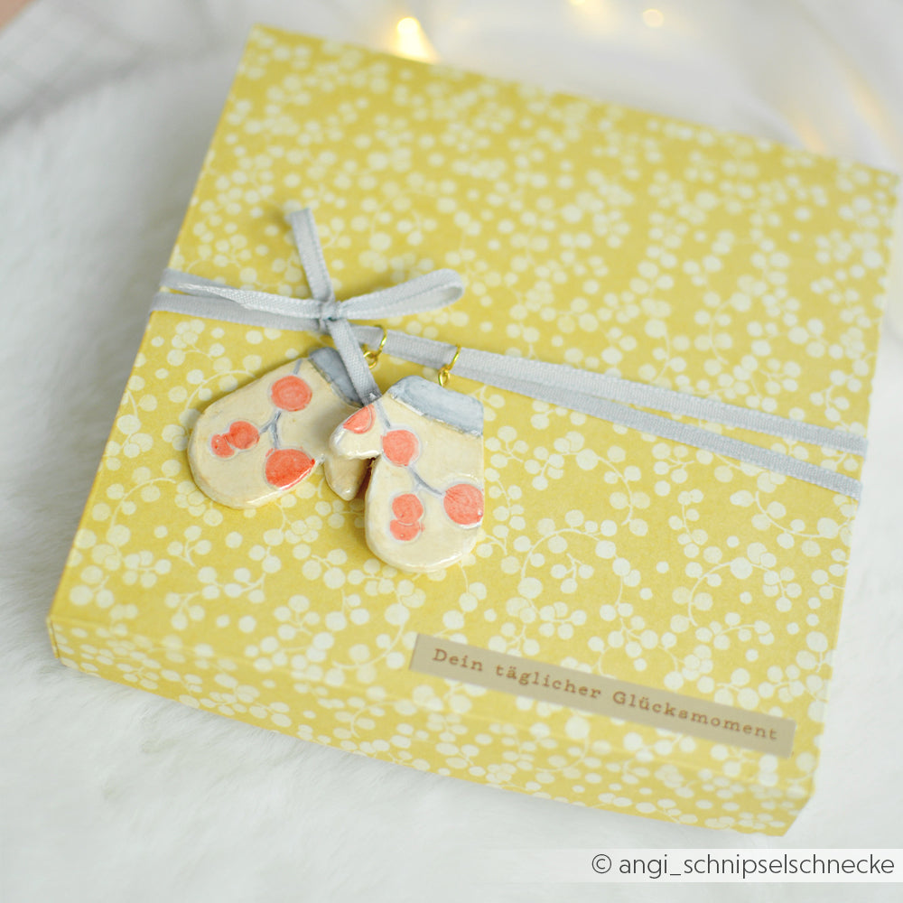 Gelbe Geschenkbox mit Schleife und zwei Anhängern aus weißer Modelliermasse, mit deutscher Beschriftung.
