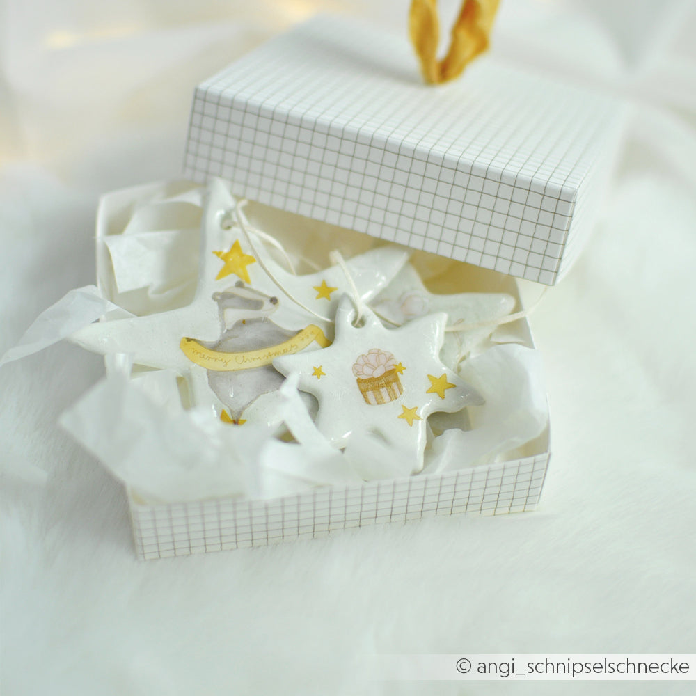 Zwei sternförmige Ornamente aus weißer, lufttrocknender Modelliermasse mit Dachs- und Geschenkmotiven.