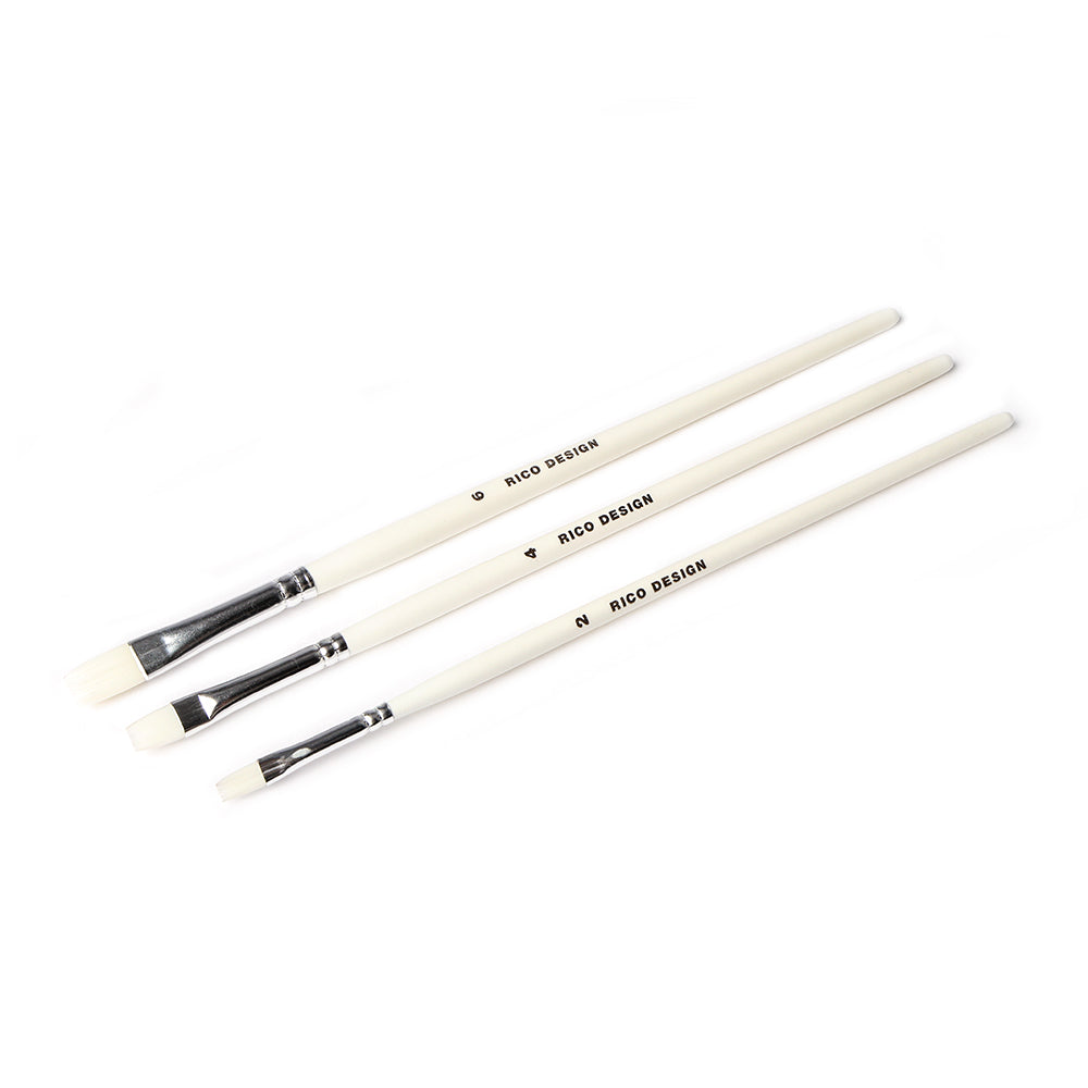 Drei Rico Design Acrylini-Pinsel mit weißem Stiel und flachen Borsten sind diagonal auf einem weißen Hintergrund angeordnet.