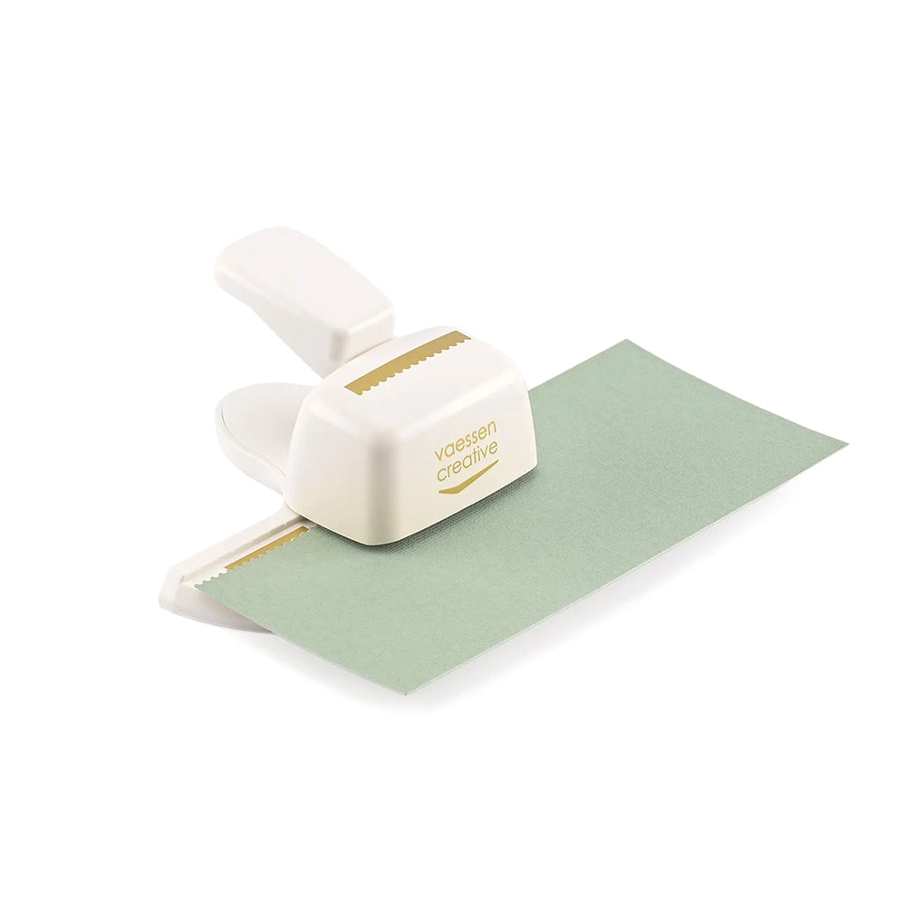 Eine Vaessen-Creative Randstanze erzeugt ein stilvolles Zickzack-Muster entlang des Randes des grünen Papiers.