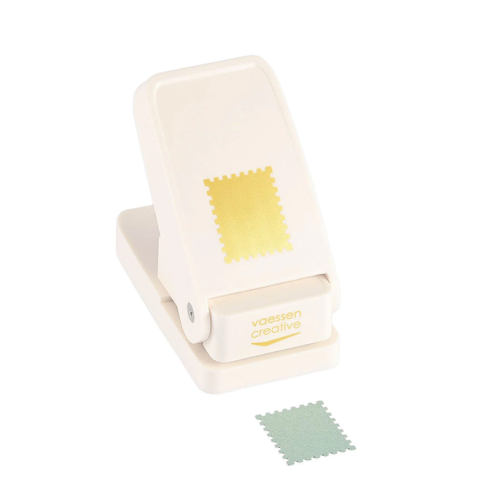Ein cremefarbener Bastelwerkzeug-Motivstanzer von Vaessen-Creative zeigt ein quadratisches Briefmarkenmotiv, neben dem ein ausgeschnittenes Papierstück liegt.