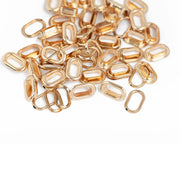 Ein Stapel kleiner, goldfarbener, ovaler Metallglieder von Vaessen liegt auf einer weißen Unterlage – ideal für Scrapbooking-Projekte. Diese Glieder, die perfekt mit den „Oval Crop-A-Dile“-Werkzeugen kompatibel sind und oft als „Metall-Ösen“ bezeichnet werden, verleihen jedem kreativen Projekt einen Hauch von Eleganz.
