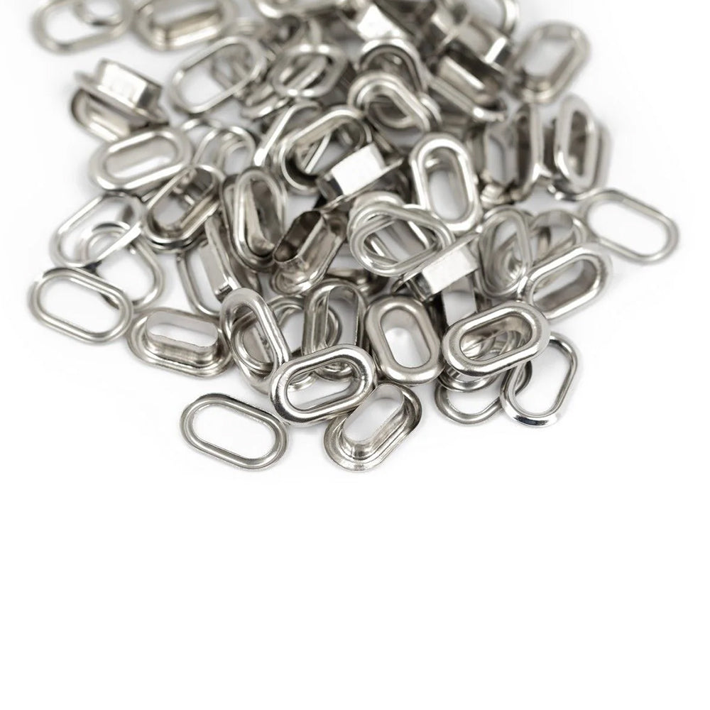 Auf einem weißen Hintergrund liegen verstreut kleine, glänzende, ovale Metallglieder von Vaessen – ideal für Scrapbooking-Projekte oder zur Verwendung mit einem „Oval Crop-A-Dile“.