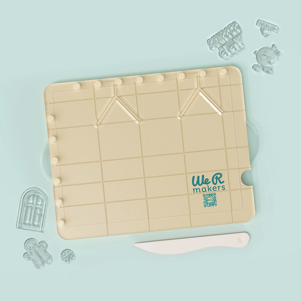 Beigefarbene Bastelplatte mit dem „We R Makers“-Logo, einem Kunststoffmesser und durchsichtigen Schablonen in Form einer Tür, eines Bären und verschiedener Figuren – ideal für einzigartige Papierbastelprojekte oder detailreiche 3D-Papierdekorationen mit der vielseitigen „Carton Stamp Board“-Platte.