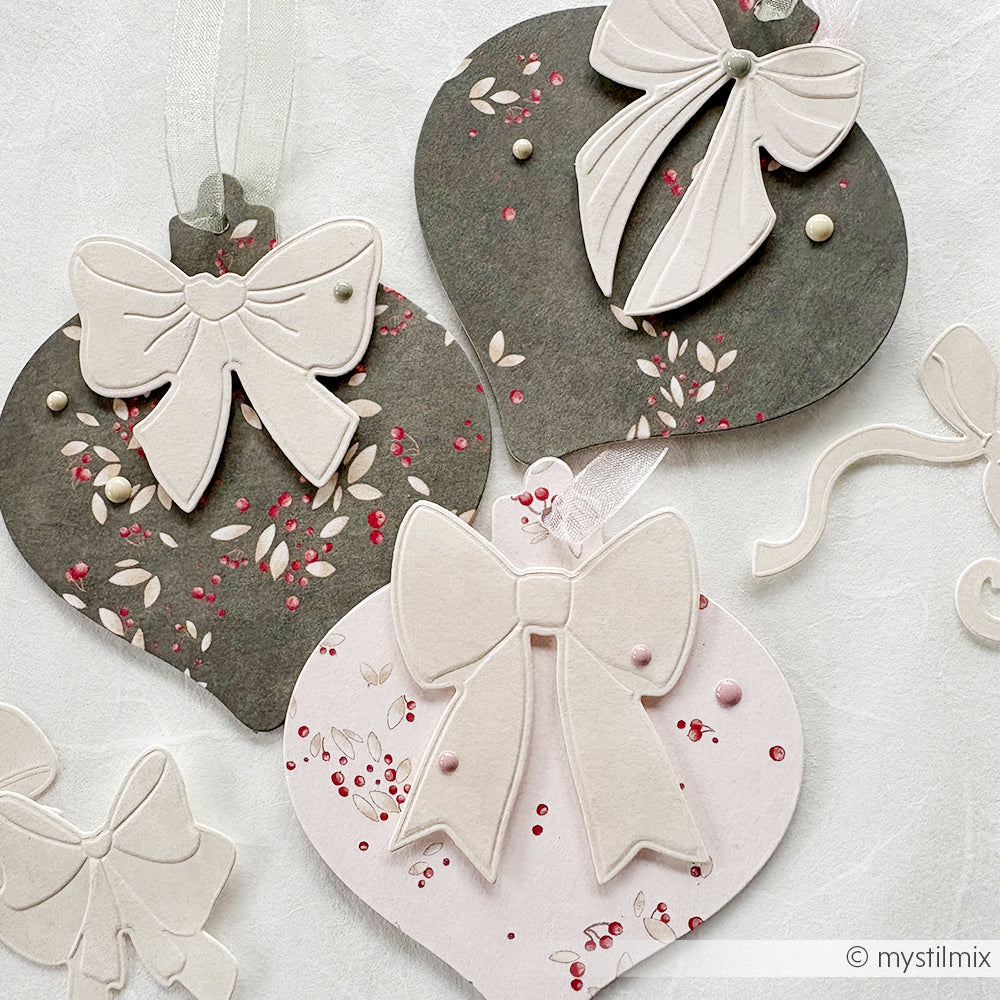 Papierornamente in Form von Kugeln von Alexandra Renke, mit PAPPcut Ornamentkugel-Techniken, weißen Schleifen und floralen Mustern, arrangiert auf einer weißen Fläche.