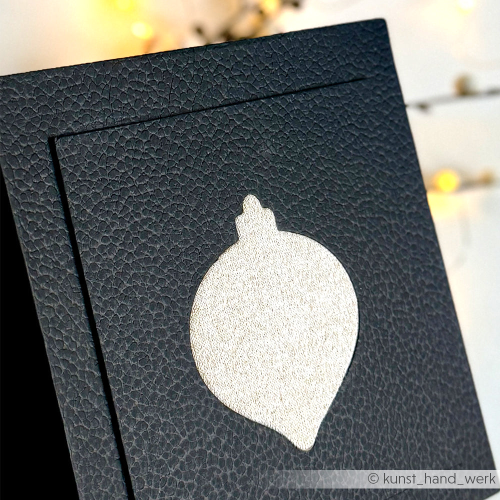 Schwarzer Strukturkarton von Alexandra Renke mit ausgeschnittener Ornamentform, beleuchtet von verschwommenen warmen Lichtern - hergestellt mit Stahlbandstanzen für präzisen PAPPcut, ideal für Buchbinderei oder kreative Projekte.