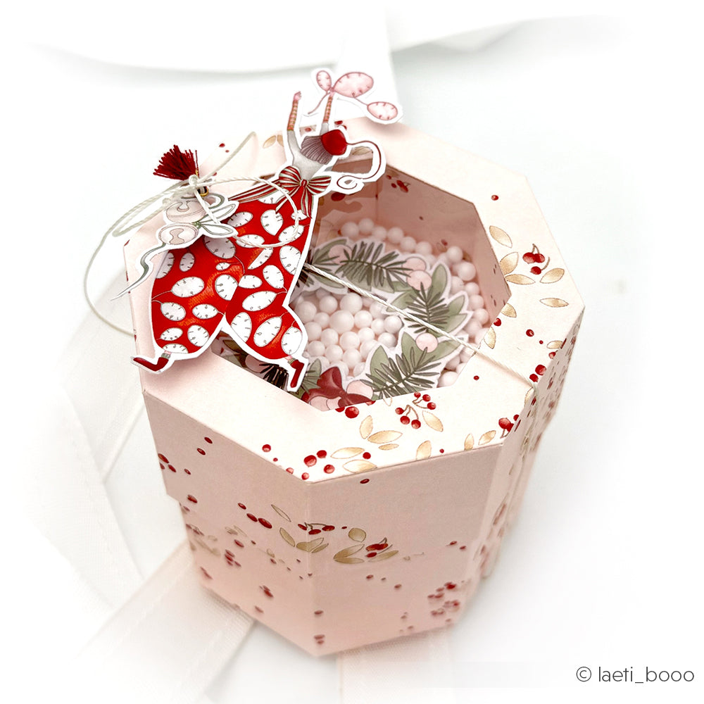 Rosafarbene achteckige Geschenkbox von Alexandra Renke mit Kirschblütenmuster und einer Ballerina-Figur, gefüllt mit weißen Perlen - ideal für Bastelprojekte mit Adventsglanz-Transferfolie oder Rub-On Figurenwelt-Akzenten.