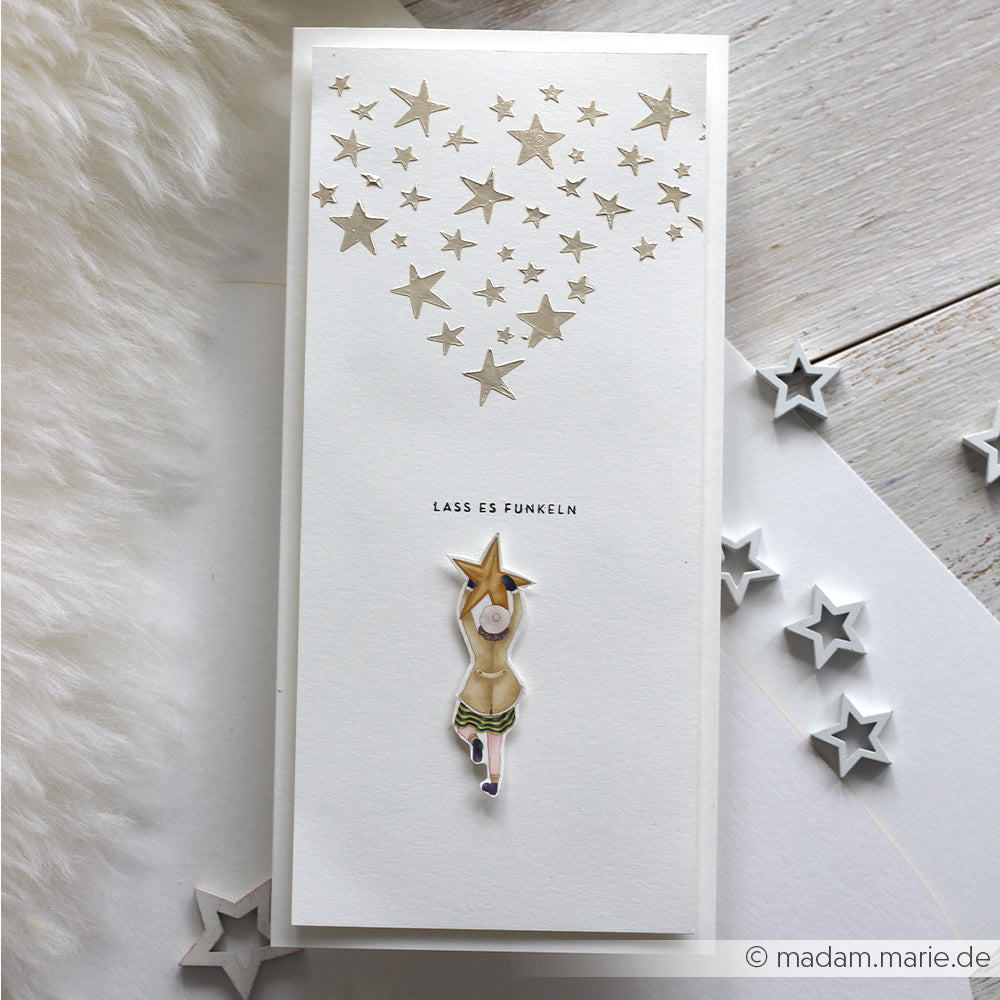 Alexandra Renke Grußkarte mit einem Mädchen und goldenen Sternen, die ein Herz mit "LASS ES FUNKELN" bilden - ideal als inspirierendes Bastelprojekte-Motiv oder in Kombination mit Rub-On Figurenwelt Sternenzauber.