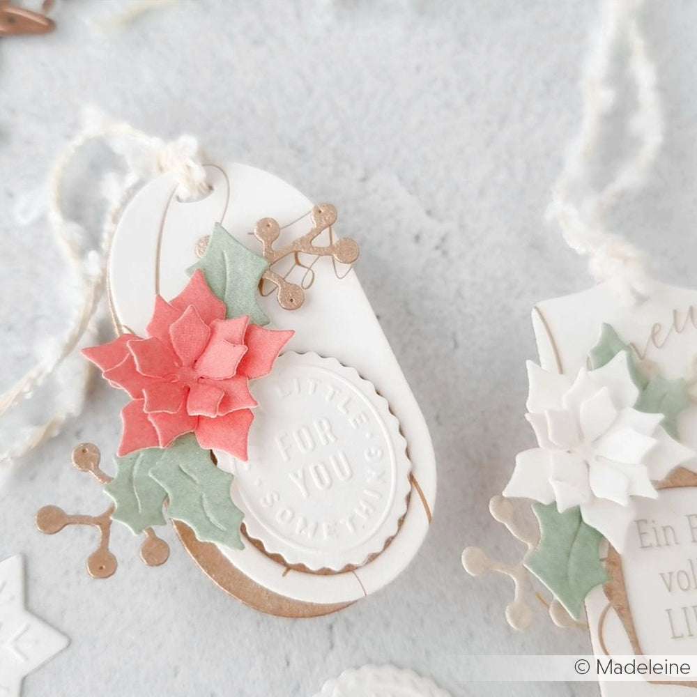 Handgefertigte Weihnachtsgeschenkanhänger von Alexandra Renke mit Weihnachtssternblüten, Stechpalmenblättern und gestempelten Botschaften auf hellem Hintergrund, hergestellt mit Cut & Emboss Folder Techniken für einzigartige Weihnachtswünsche.