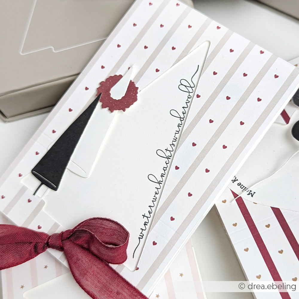 Grußkarte von Alexandra Renke mit einer Gnom-Illustration, einem Herzmuster, einem weinroten Band und einem kursiven Text auf einem gestreiften Hintergrund - ideal für Sammler oder Fans von kreativen Papierbasteleien.