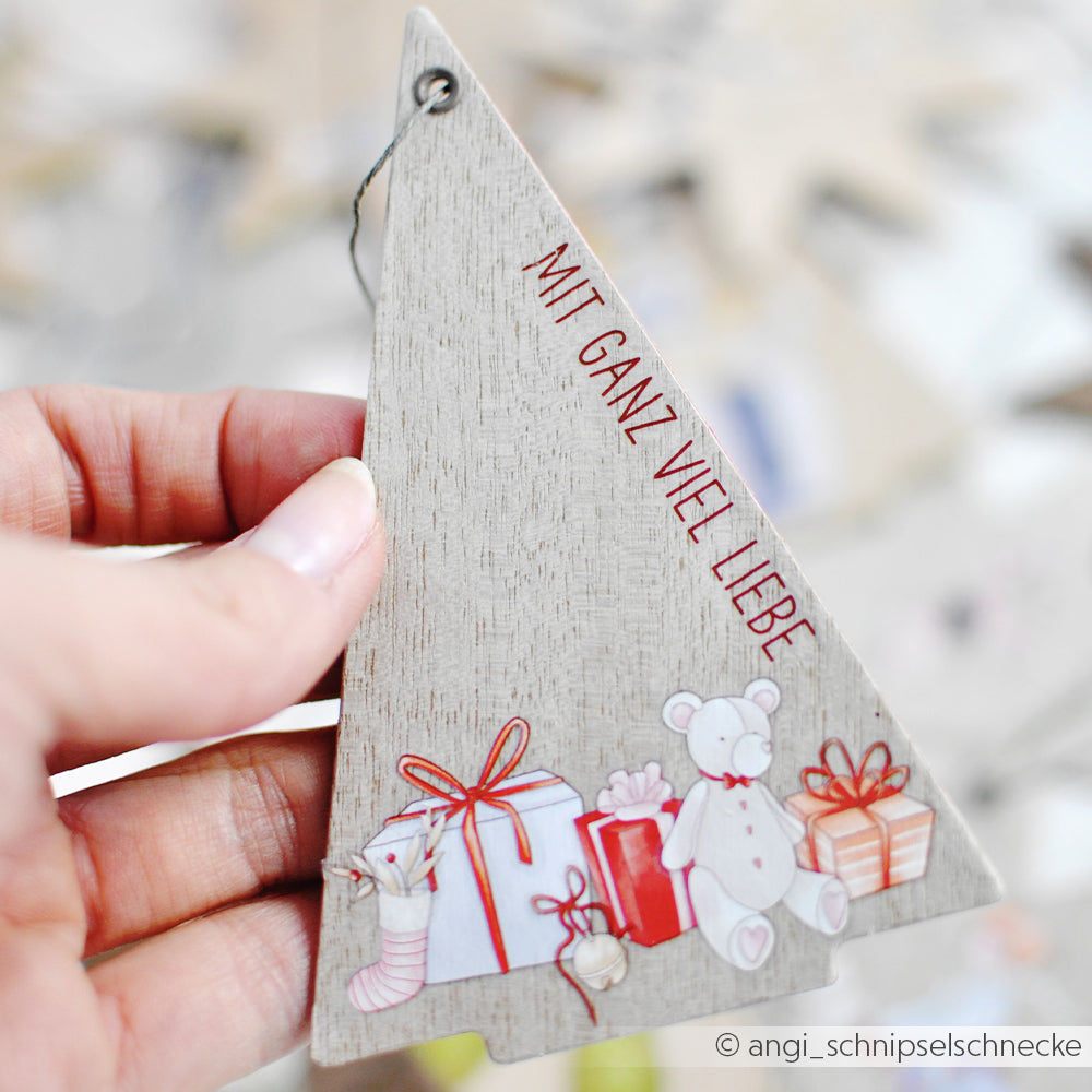 Eine Hand hält eine hölzerne Alexandra Renke PAPPcut Tanne mit Geschenken, einem Teddybär und dem Text "MIT GANZ VIEL LIEBE".