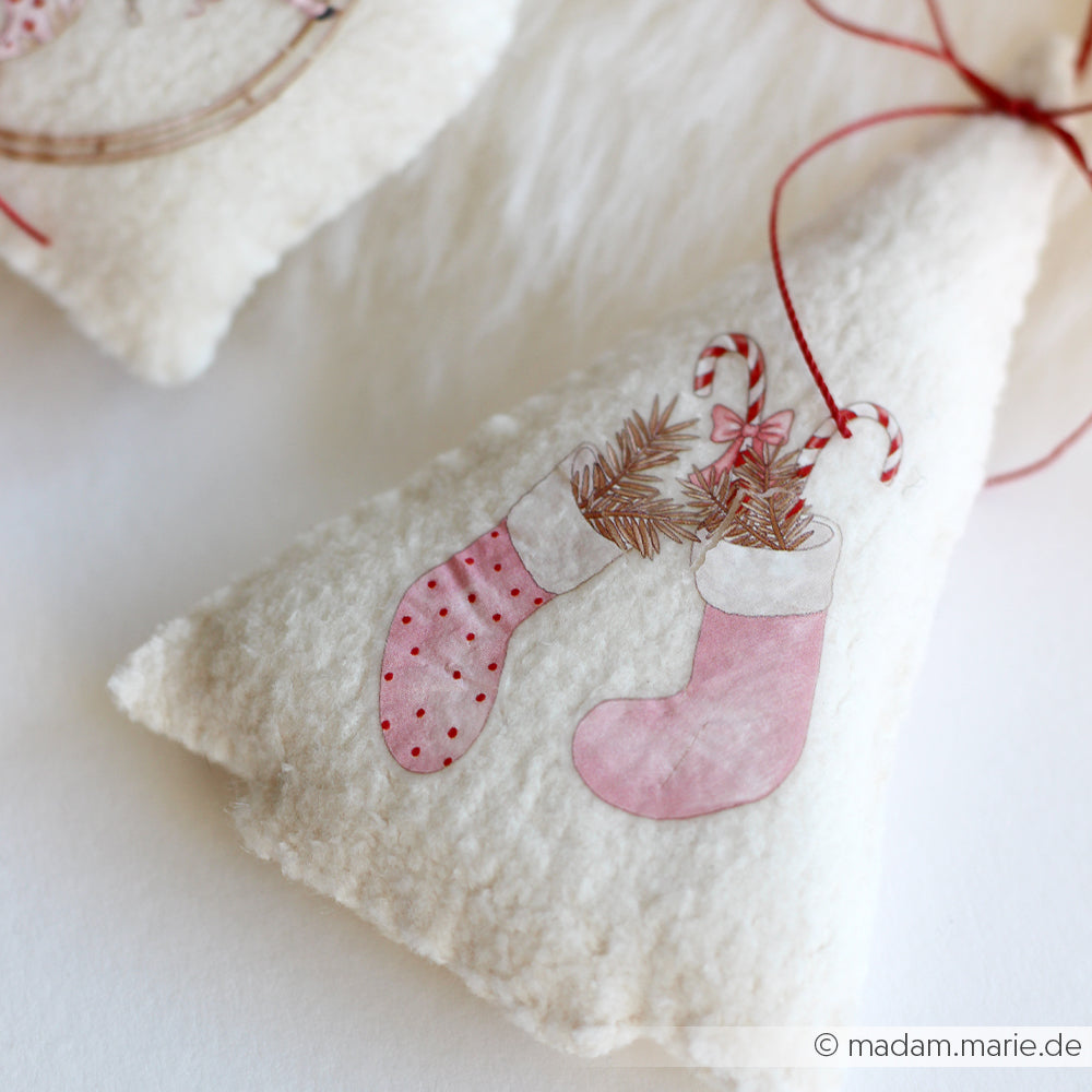 Ornament aus cremefarbenem Filz mit zwei rosafarbenen Strümpfen, Zuckerstangen und Tannenzweigen, die mit roter Schnur zusammengebunden sind. Das Ornament wurde mit der Buchbindentechnik hergestellt und von den PAPPcut Tanne-Entwürfen von Alexandra Renke inspiriert.